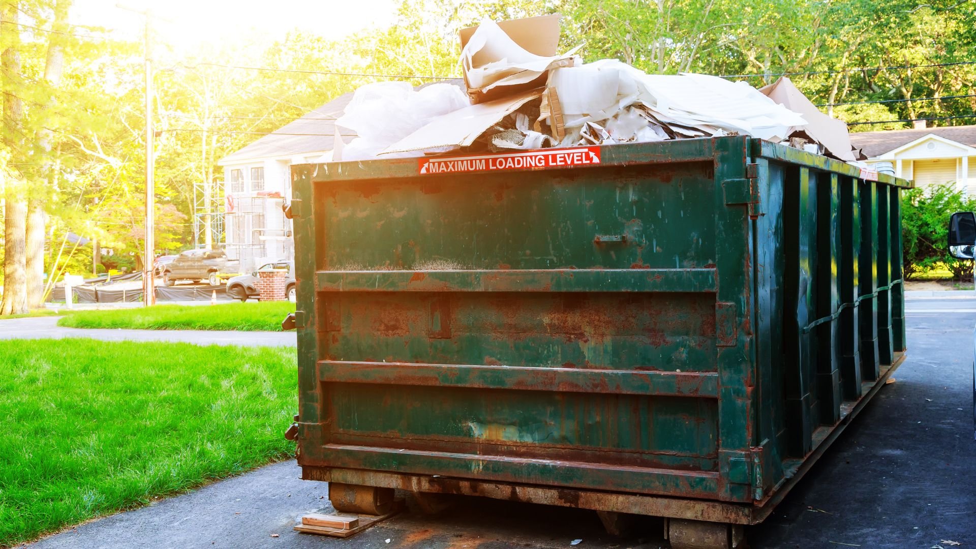 Overflowing green dumpster on residential street with debris and maximum loading sign