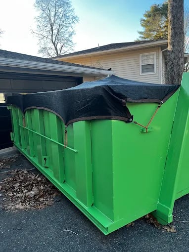 Green dumpster with black tarp cover parked near residential house