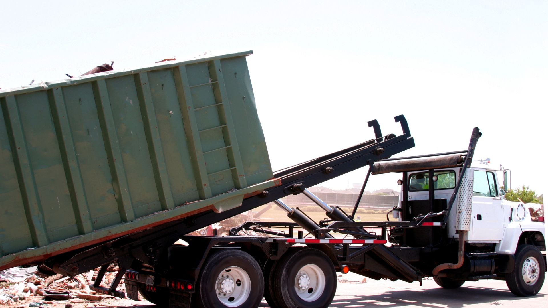 White roll-off truck lifting a large green dumpster at construction site