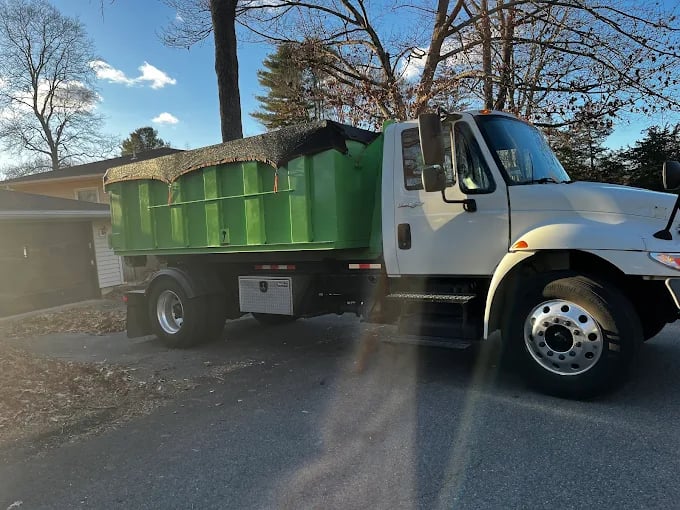 Green dumpster truck parked on residential street on a sunny day