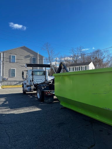 Green dumpster and truck on residential street on sunny day