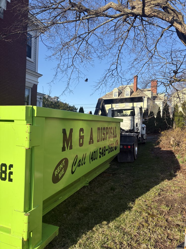 Bright green M & A Disposal dumpster truck parked near residential buildings