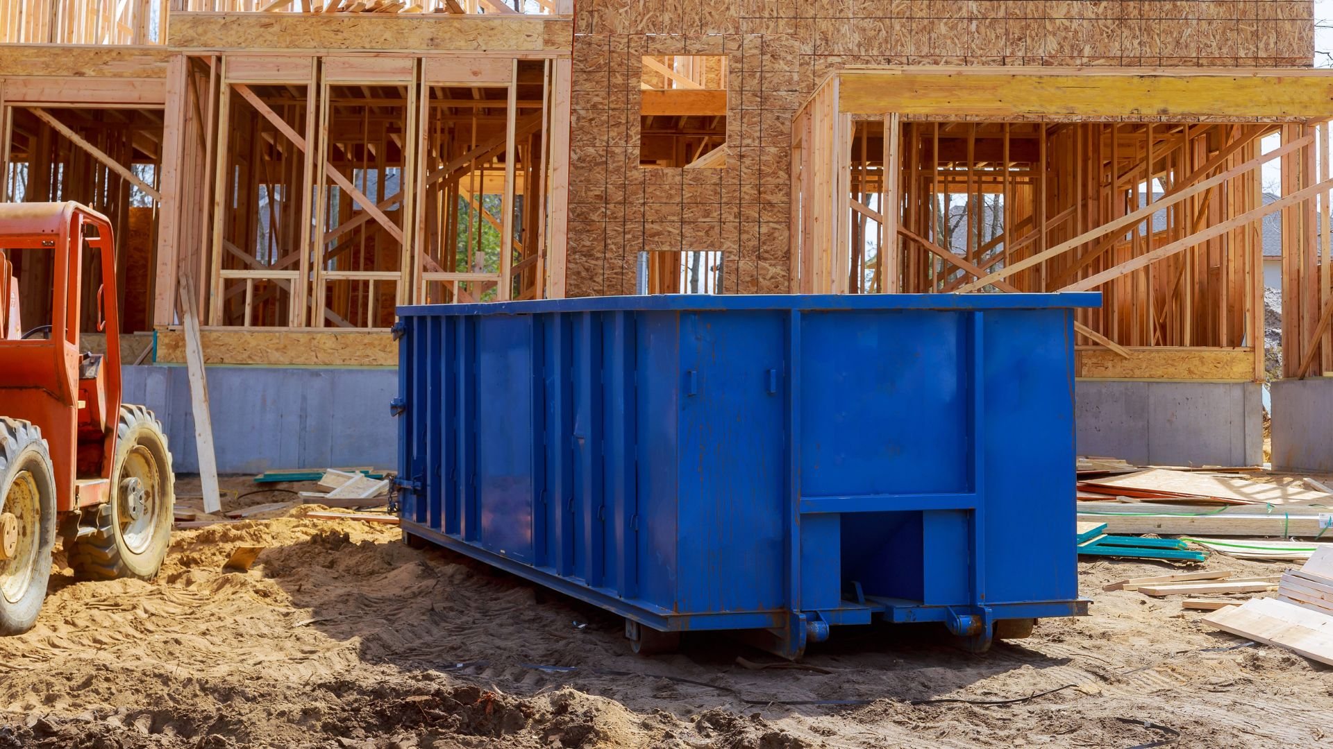 Blue dumpster at residential construction site with wooden framing