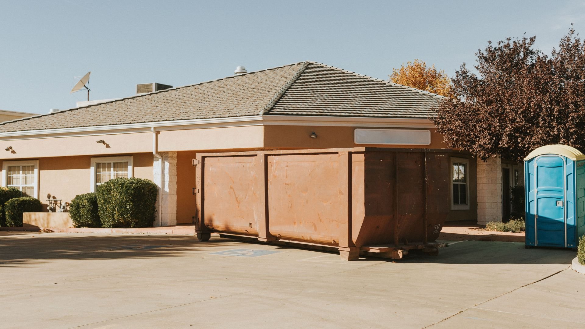 Commercial building with dumpster and portable toilet on concrete parking lot