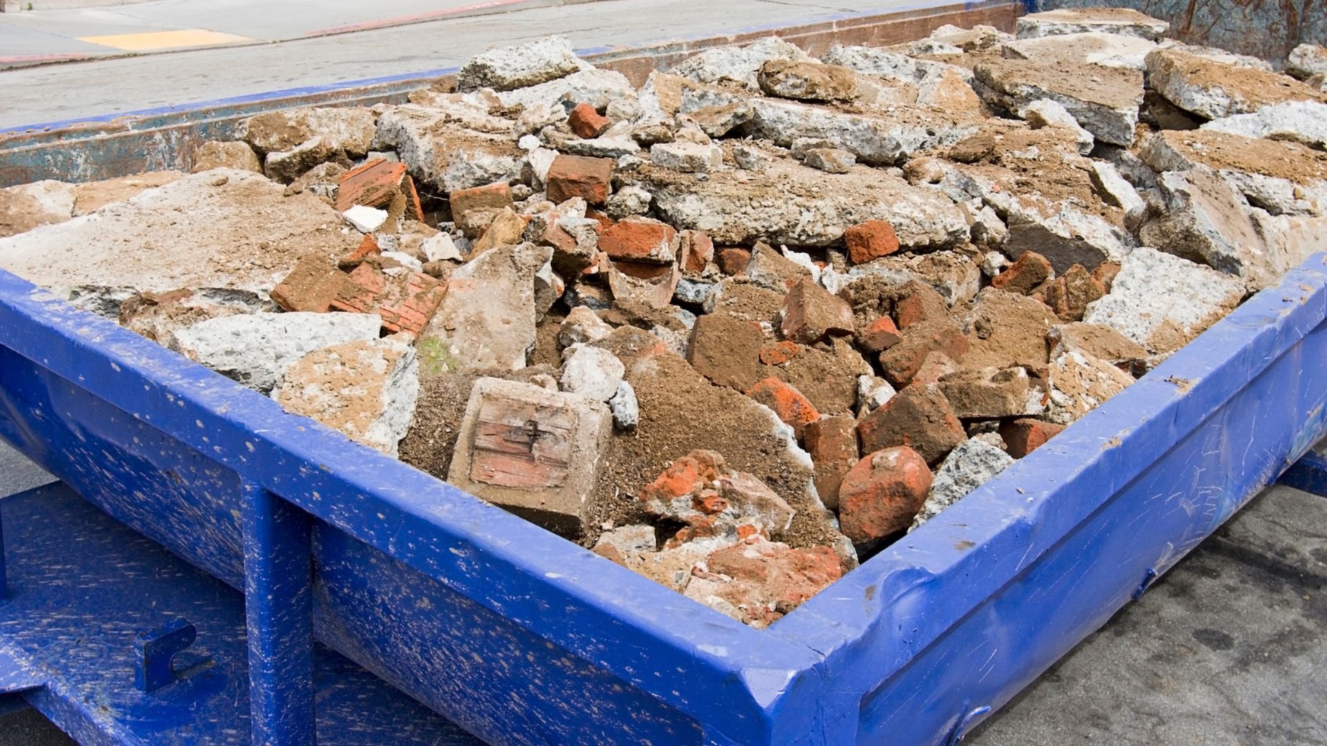 Blue construction dumpster filled with broken bricks, concrete, and construction debris